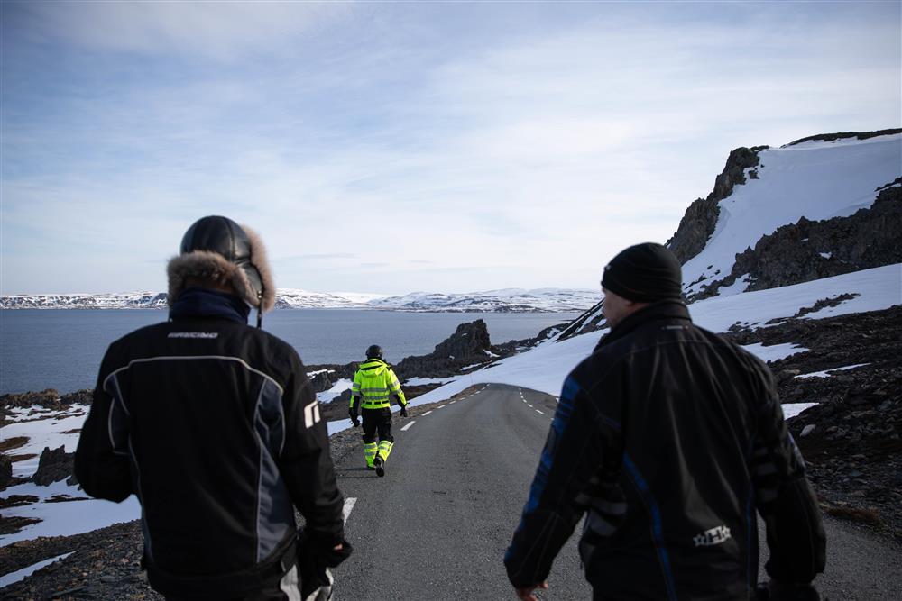 Tre godt kledde mennesker går nedover en landevei i arktisk vinterlandskap. - Klikk for stort bilde