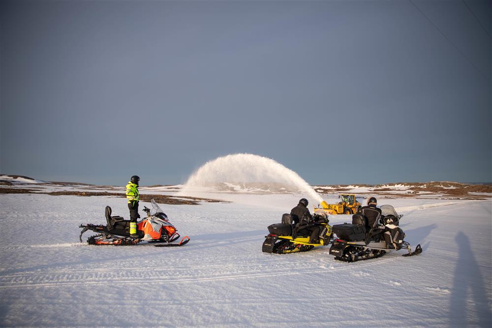 Tre skutere med førere står nysgjerrig ved en stor snøfreser. En stor søyle med snø er synlig.  - Klikk for stort bilde