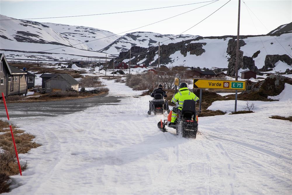 To skutere kjører gjennom et lite hyttefelt i et landeveiskryss. - Klikk for stort bilde