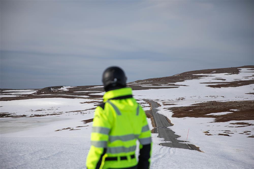 En mann i varselgul jakke skuer utover et arktisk vinterlandskap. - Klikk for stort bilde